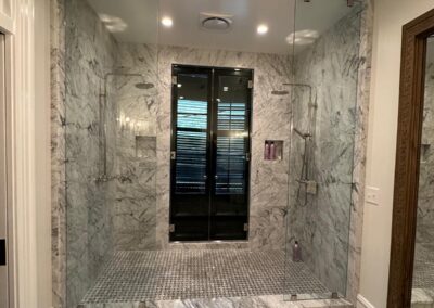 Custom walk-in shower clad in marble-look tile with a dark glass door
