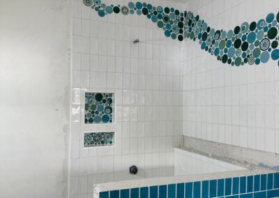 Teal tiled tub surround with a mosaic border above