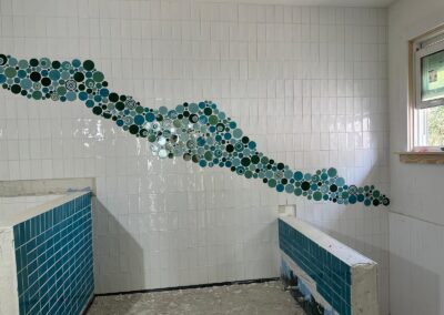 Teal glass mosaic wave feature running across white subway tile